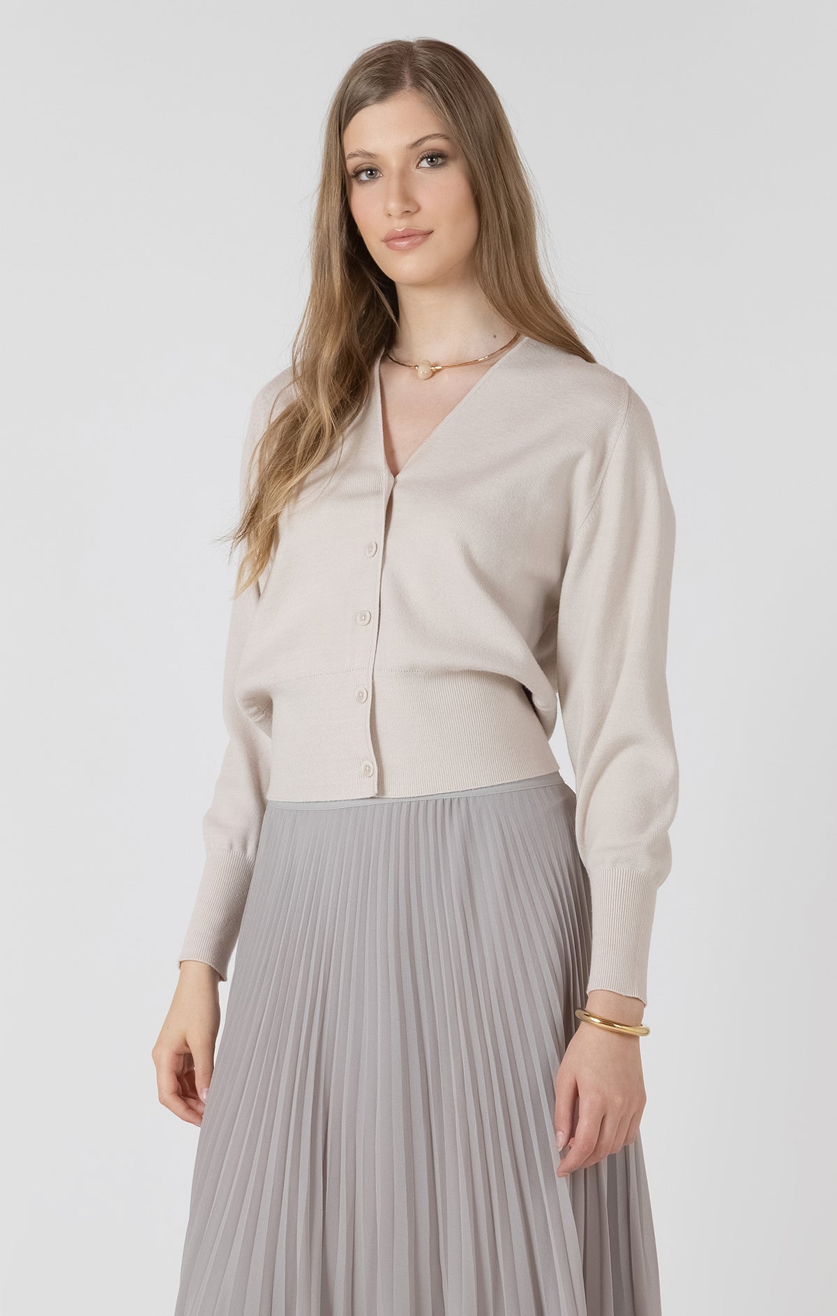 Cardigan beige porté avec une jupe plissée