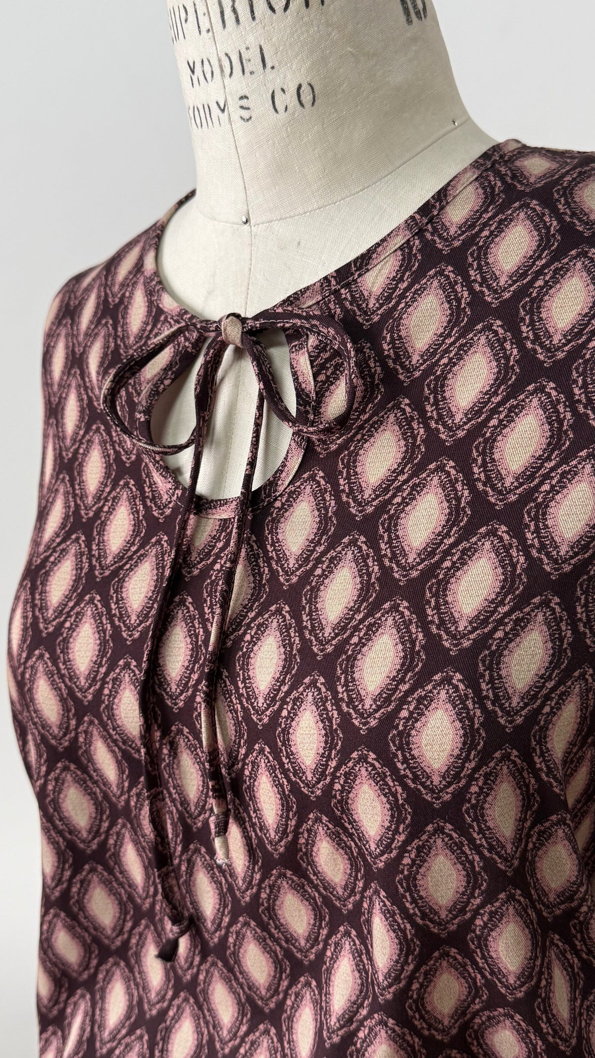 Blouse Isabella en viscose à imprimé géométrique marron et rosé, avec col rond et nouet délicat.