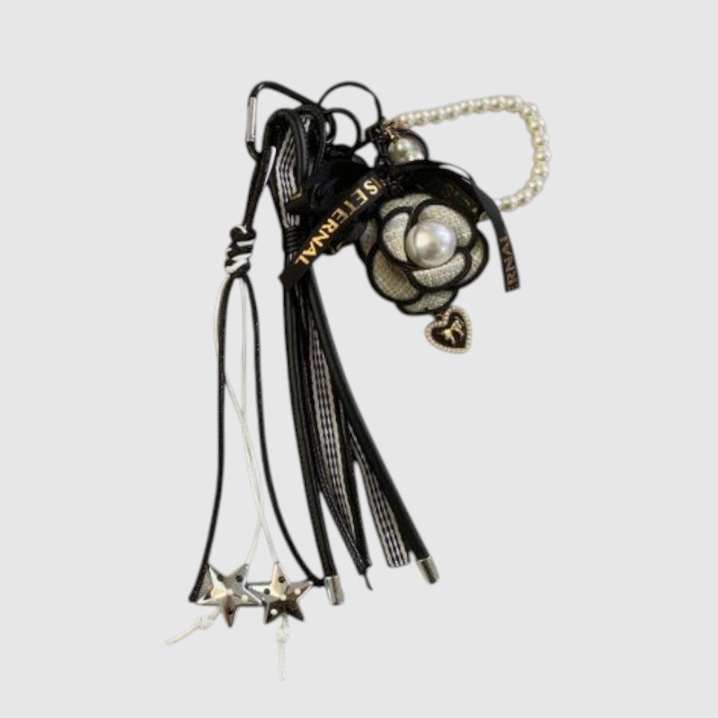 Breloque de sac – Fleur noire et nacrée. Fleur noire et crème à centre nacré, perles décoratives, franges et petites étoiles suspendues.