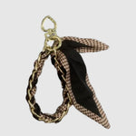 Breloque de sac – Foulard pied-de-poule brun. Chaîne dorée entrelacée d’un foulard noir et brun à motif pied-de-poule, avec attache en forme de cœur.