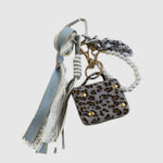 Breloque de sac – Mini-sac léopard gris. Mini-sac décoratif à motif léopard gris, rubans bleu pâle, dentelle et perles décoratives.