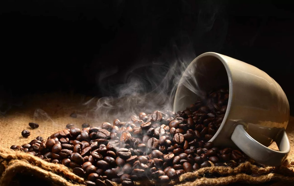 Grains de café torréfiés devant une tasse renversée, avec de la vapeur