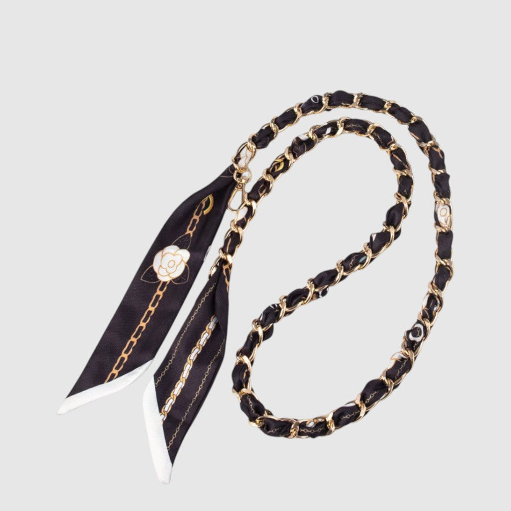 Courroie de téléphone – Foulard noir et doré. Chaîne de couleur dorée entrelacée d’un foulard noir à motifs, prolongé par deux pans décoratifs.