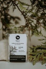 Boîte de pastilles de cire Nature Mulâne, devant des branches de cèdre