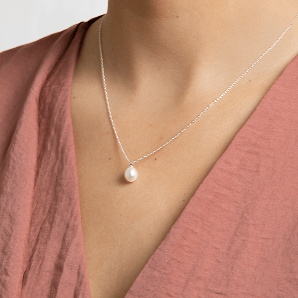 Collier doré avec perle blanche porté sur un haut rose