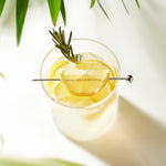 Pique à cocktail Final Touch posée sur un verre garni de citron et de romarin.