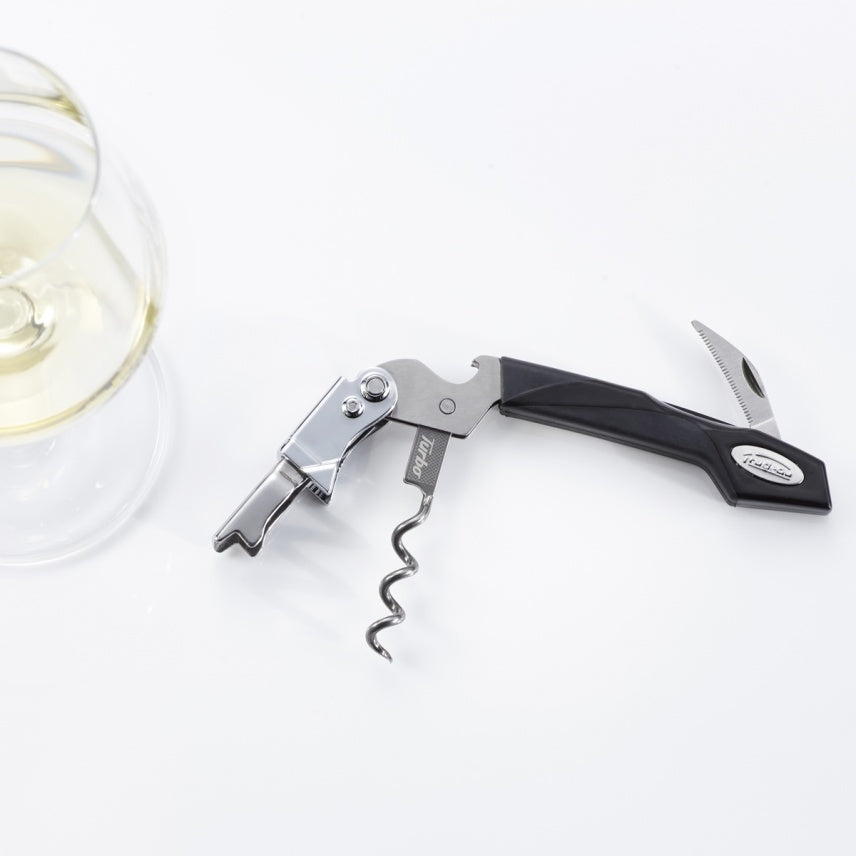Tire-bouchon Turbo Trudeau ouvert à côté d’un verre à vin